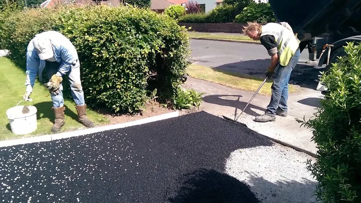 Crew raking new asphalt along the edge of a driveway