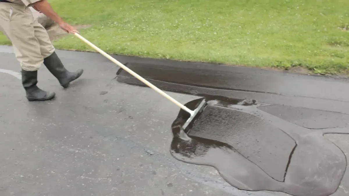 Sealer being spread across an asphalt driveway with a squeegee